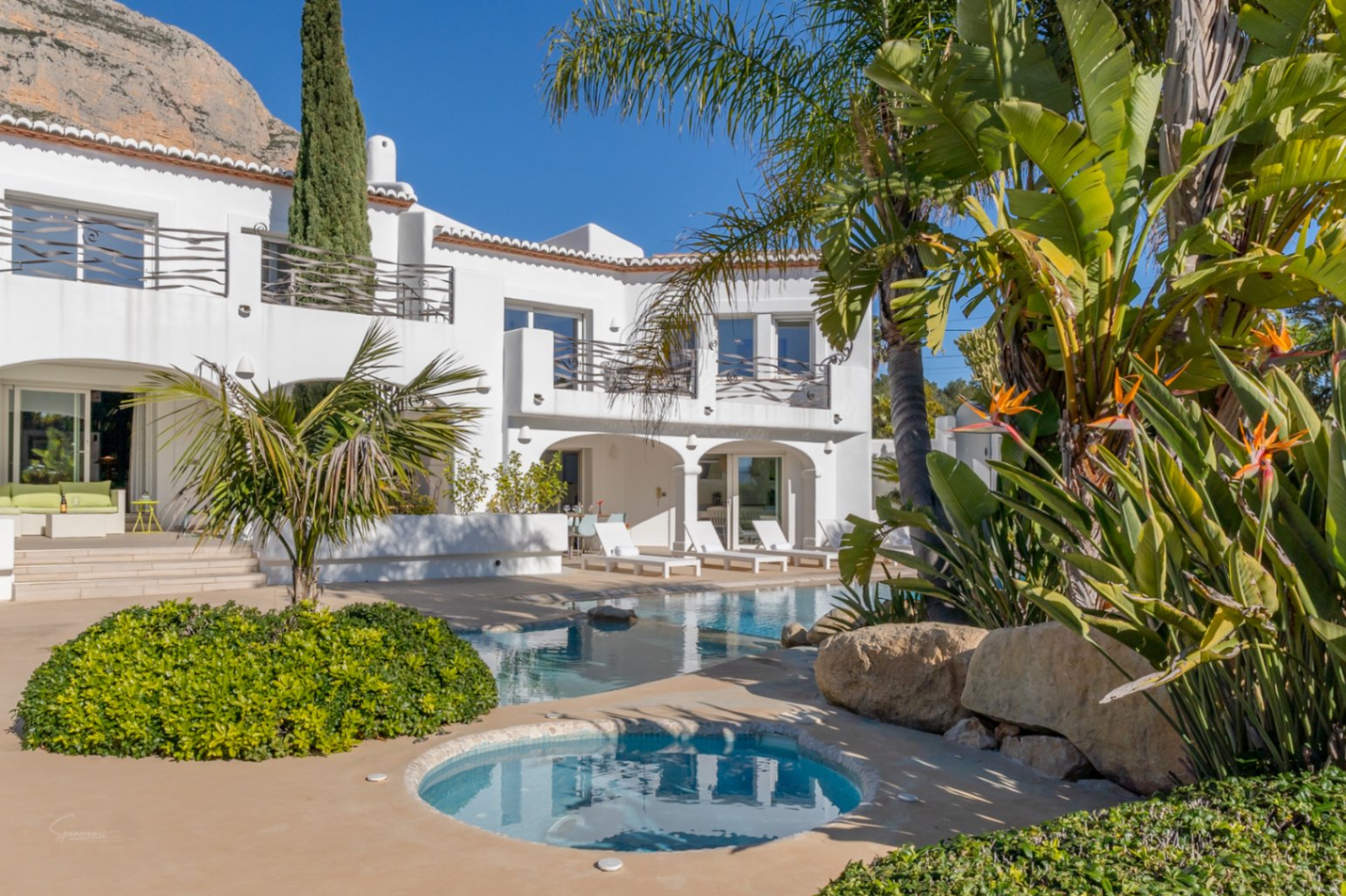 Ibiza-style villa exterior featuring a designer pool with integrated jacuzzi, arched naya, and upper terraces against the backdrop of the Montgó mountain.