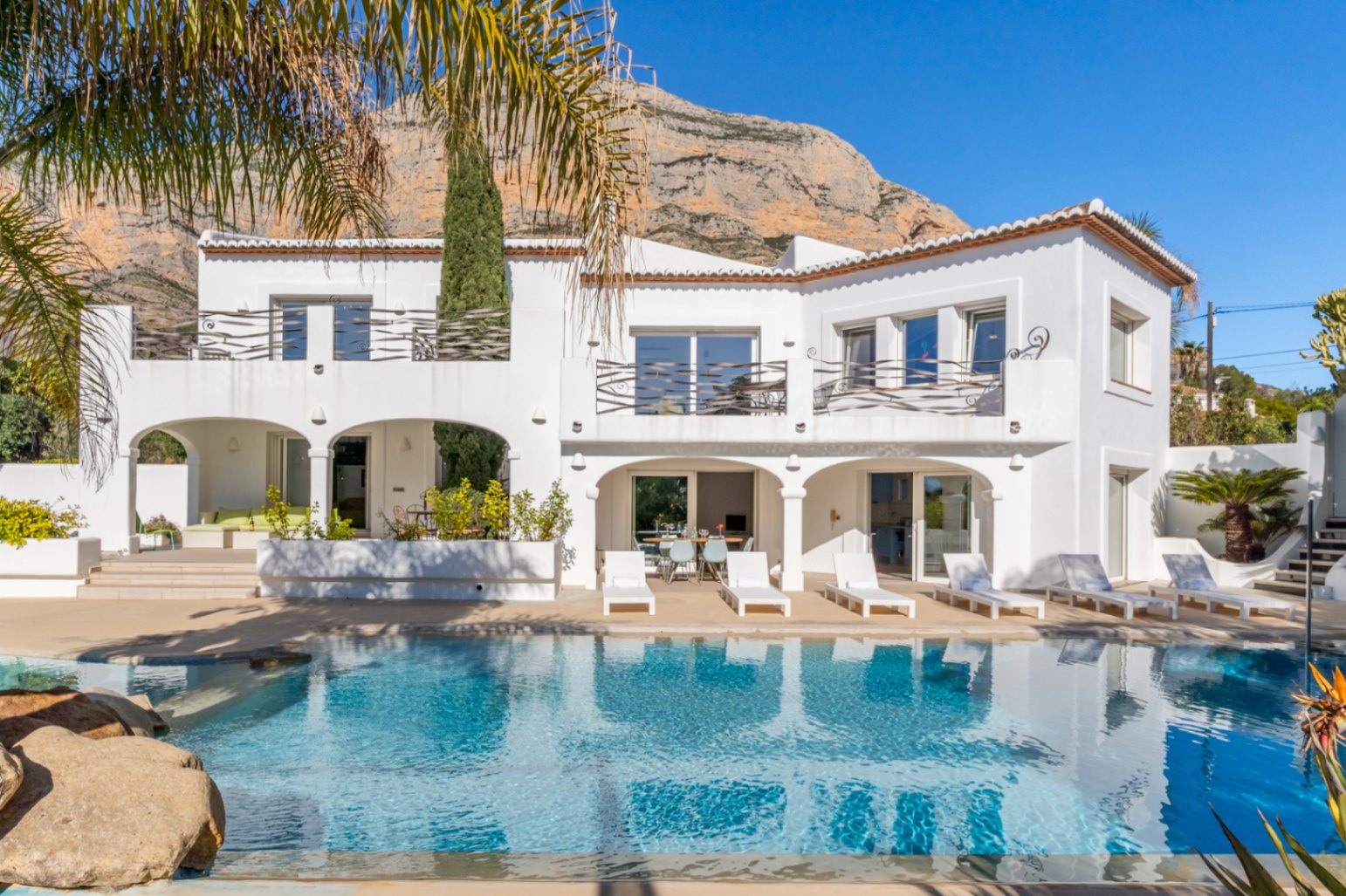Ibiza-style white facade featuring a swimming pool, arched naya, and upper terraces set against the majestic Montgó mountain.
