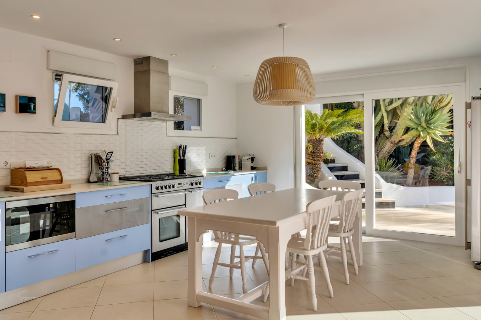 Modern kitchen with pastel blue cabinetry, a white wooden dining suite, and sliding glass doors that offer seamless access to the sun-drenched patio.