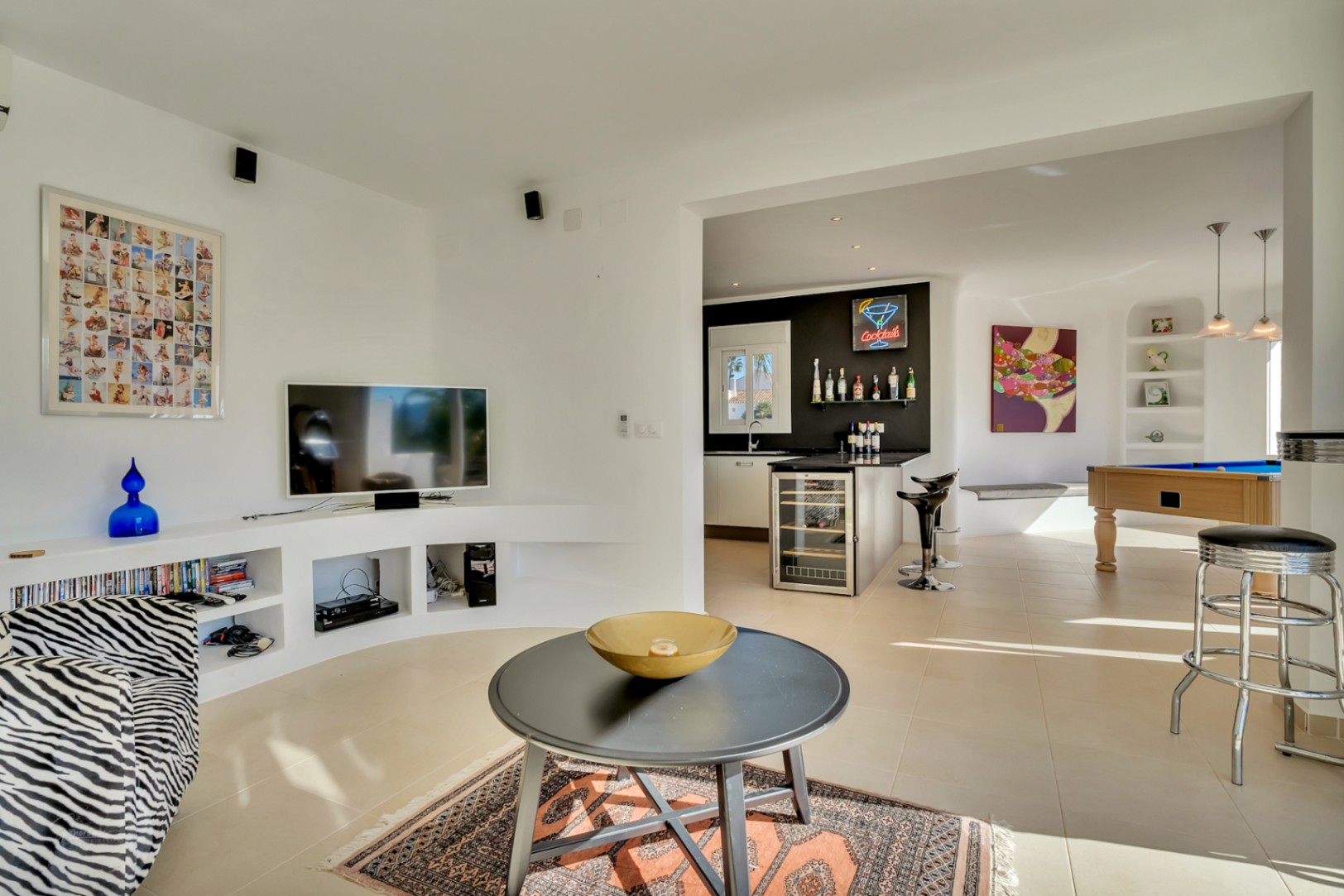 Open-concept living room featuring a curved built-in media shelf, a sleek bar with wine cooler, and an entertainment area with a pool table.