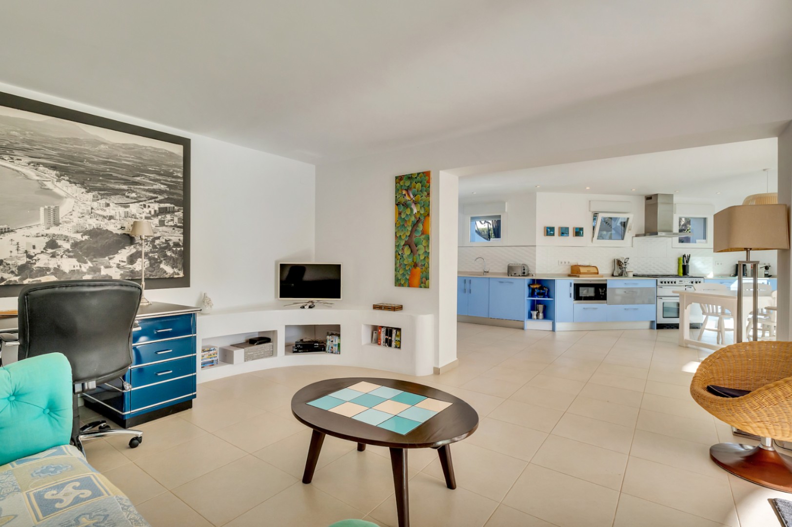 Open-plan living space featuring a dedicated office area, built-in curved shelving, and a seamless transition to a modern kitchen with blue cabinetry.