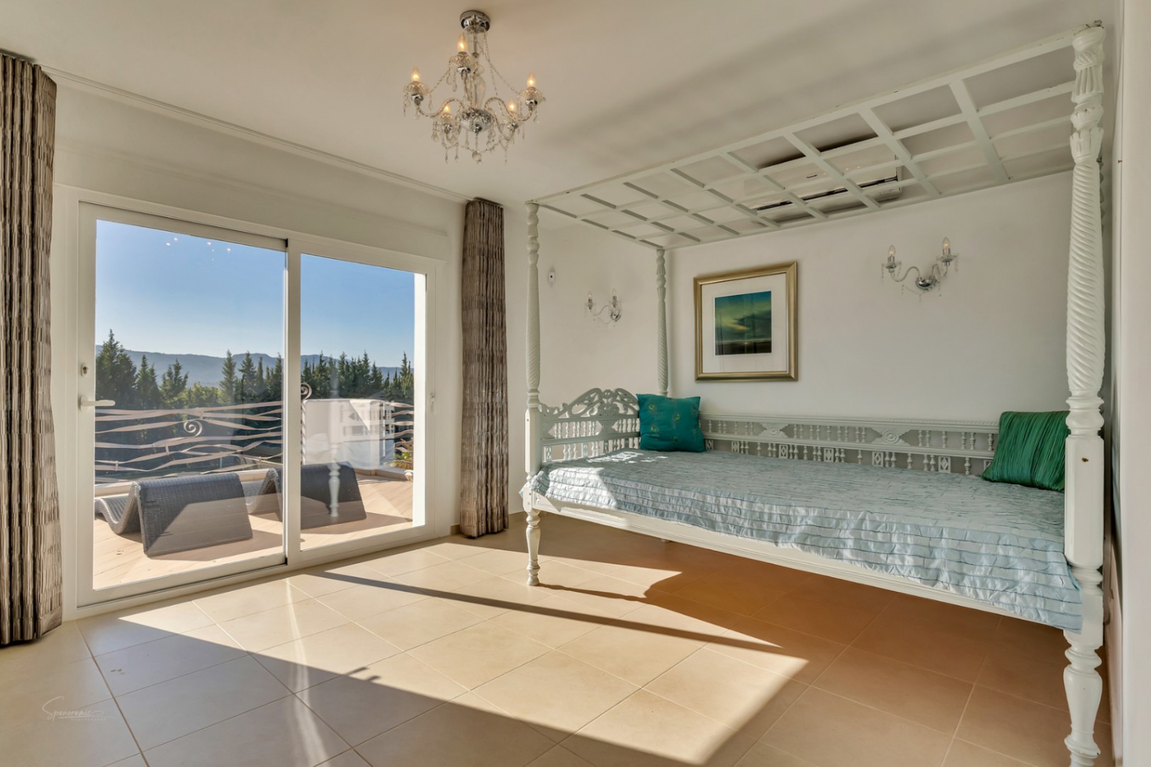 Spacious bedroom featuring an ornate white four-poster bed and direct access to a sun-drenched terrace with panoramic mountain views.