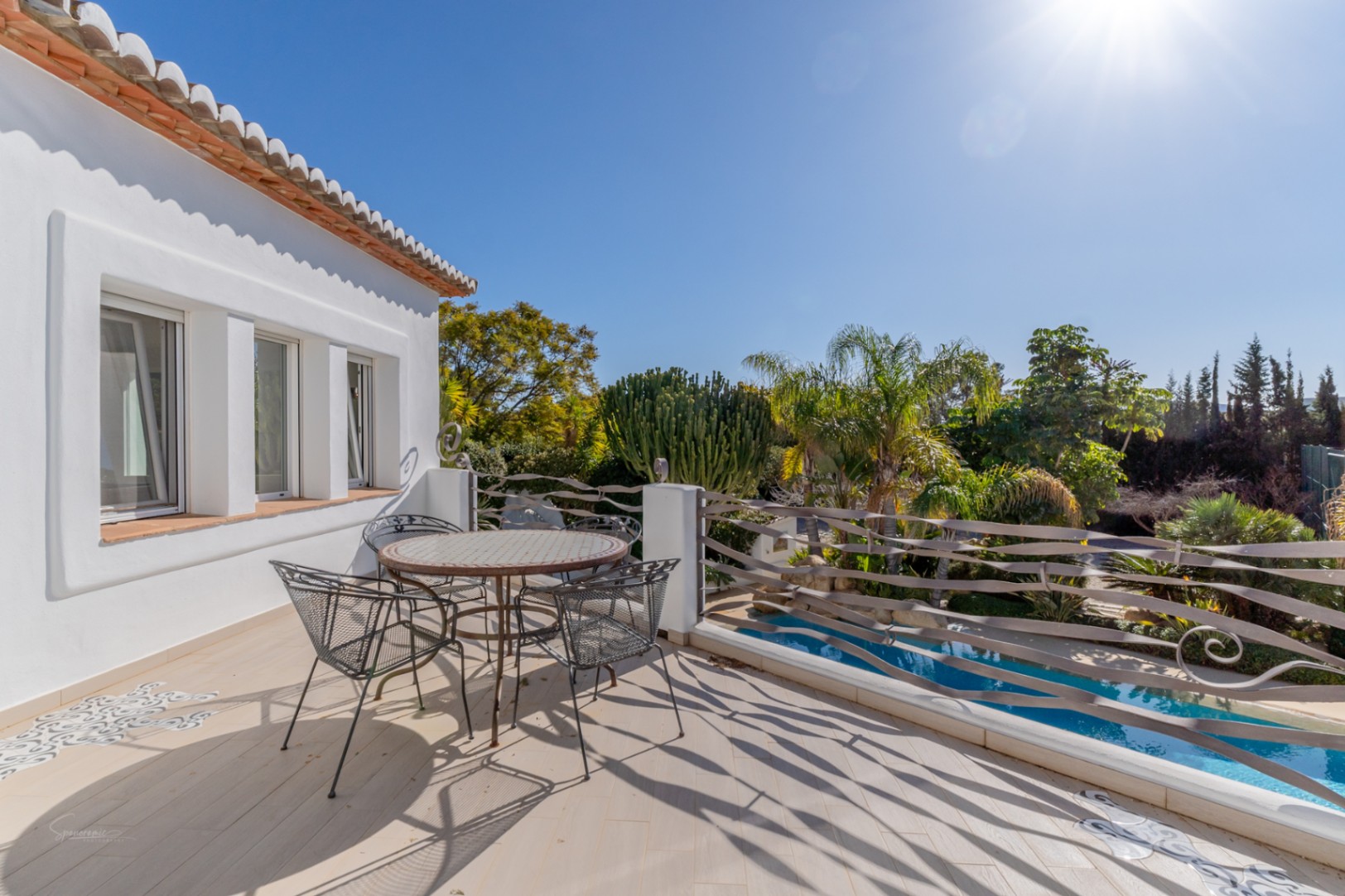 Upper terrace featuring a mosaic-topped table, wavy metal railings, and tiled flooring with decorative inserts, overlooking the swimming pool and lush tropical gardens.