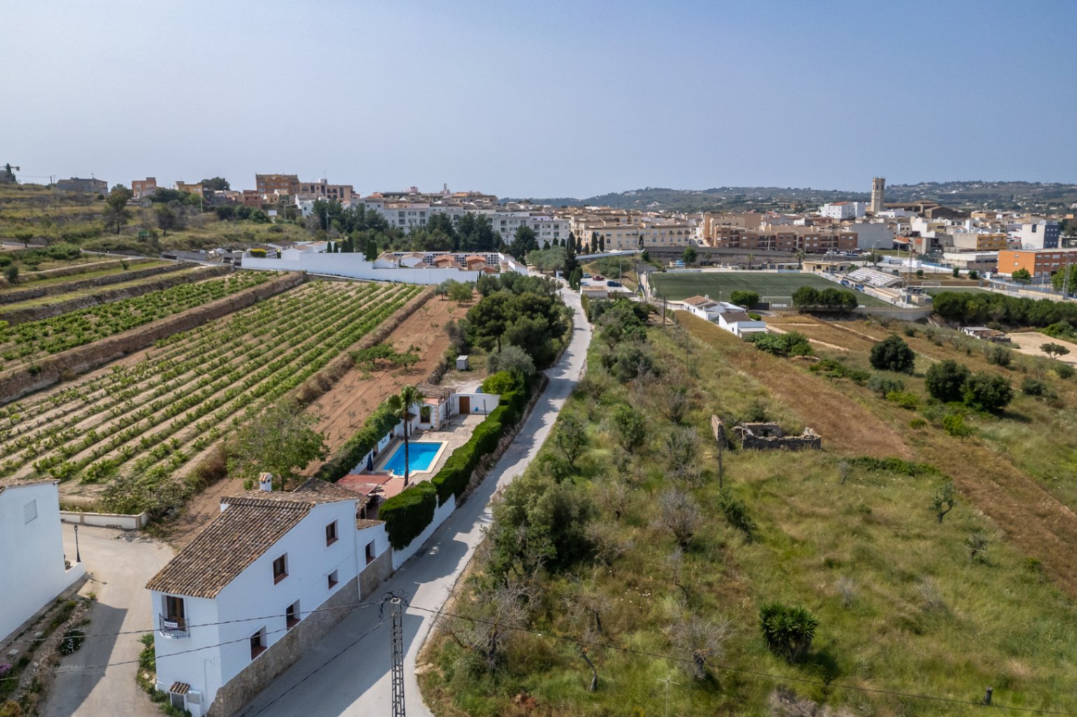 Aerial view of a country house with pool in Teulada, surrounded by vineyards and Mediterranean vegetation.