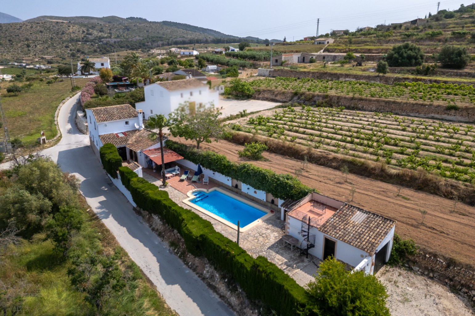 Aerial view of a finca with a blue pool, mature garden, and cultivated fields in Teulada, Costa Blanca.
