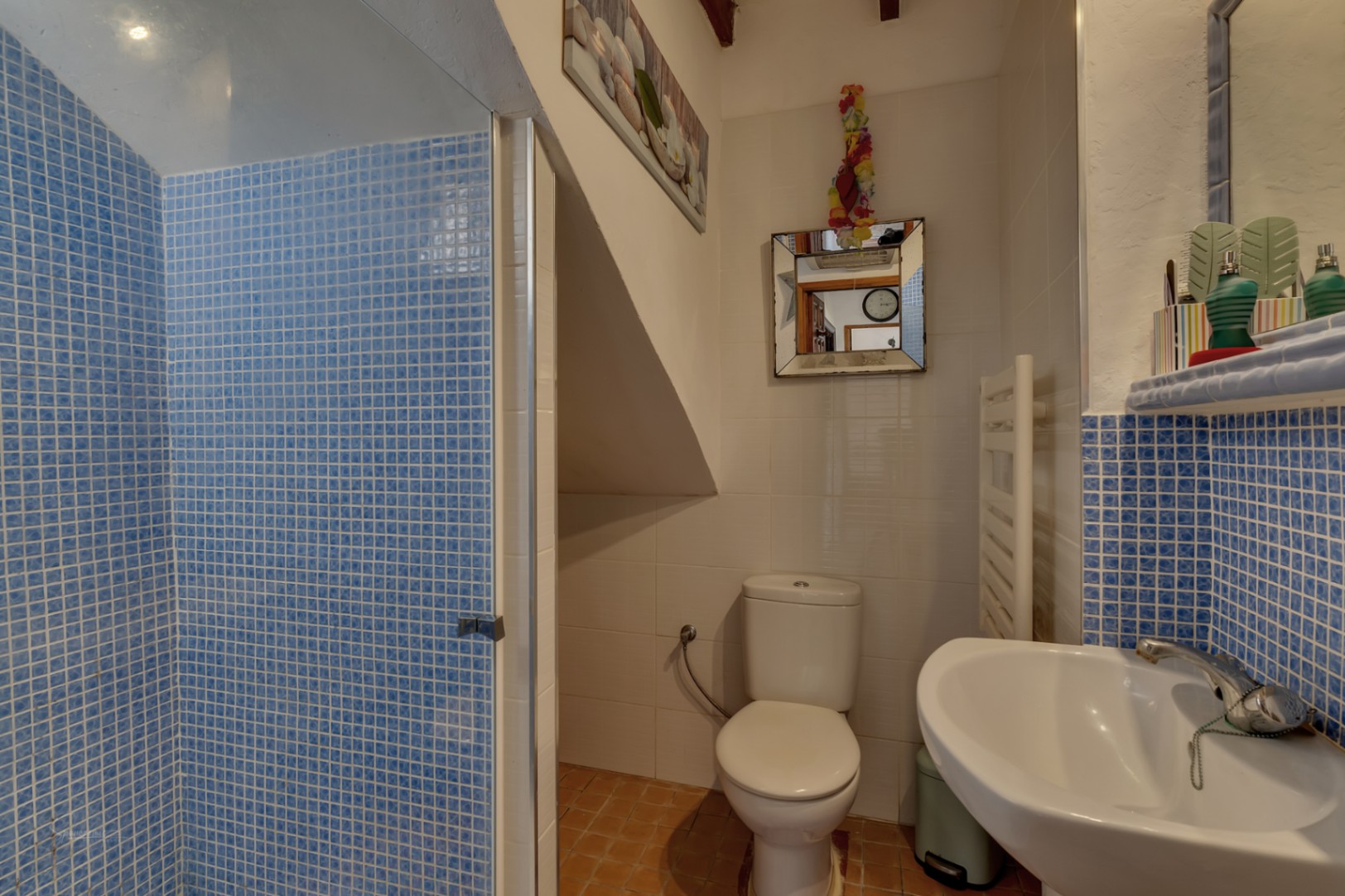 Bathroom detail with blue mosaic shower, white toilet, and sink with mosaic countertop.