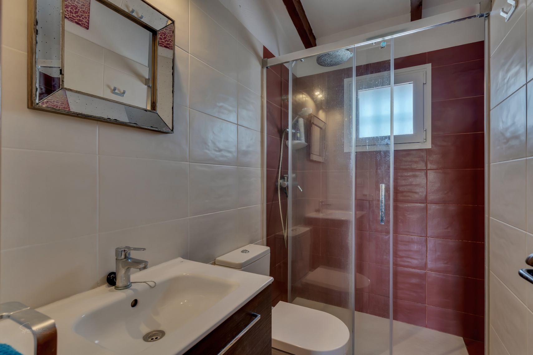 Bathroom detail with glass shower, modern sink, and tile in neutral and burgundy tones.