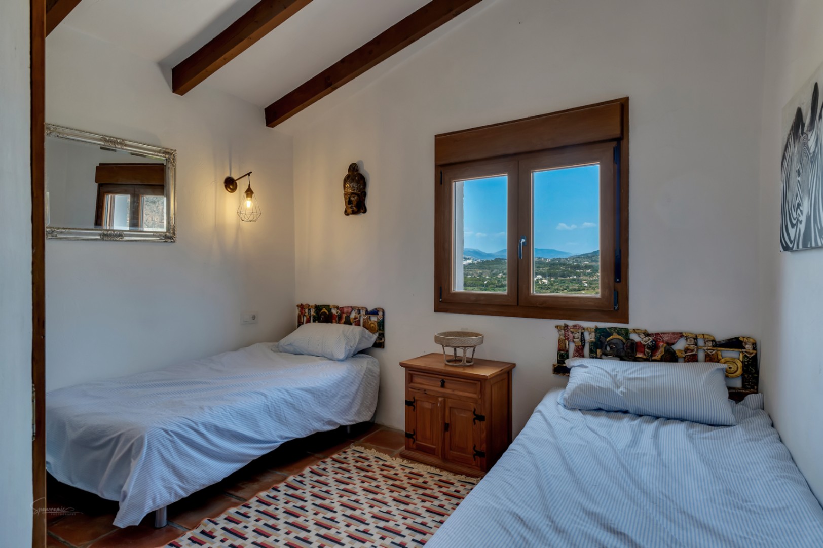 Bedroom with twin beds, exposed wood beams, and landscape views from the wood-framed window.
