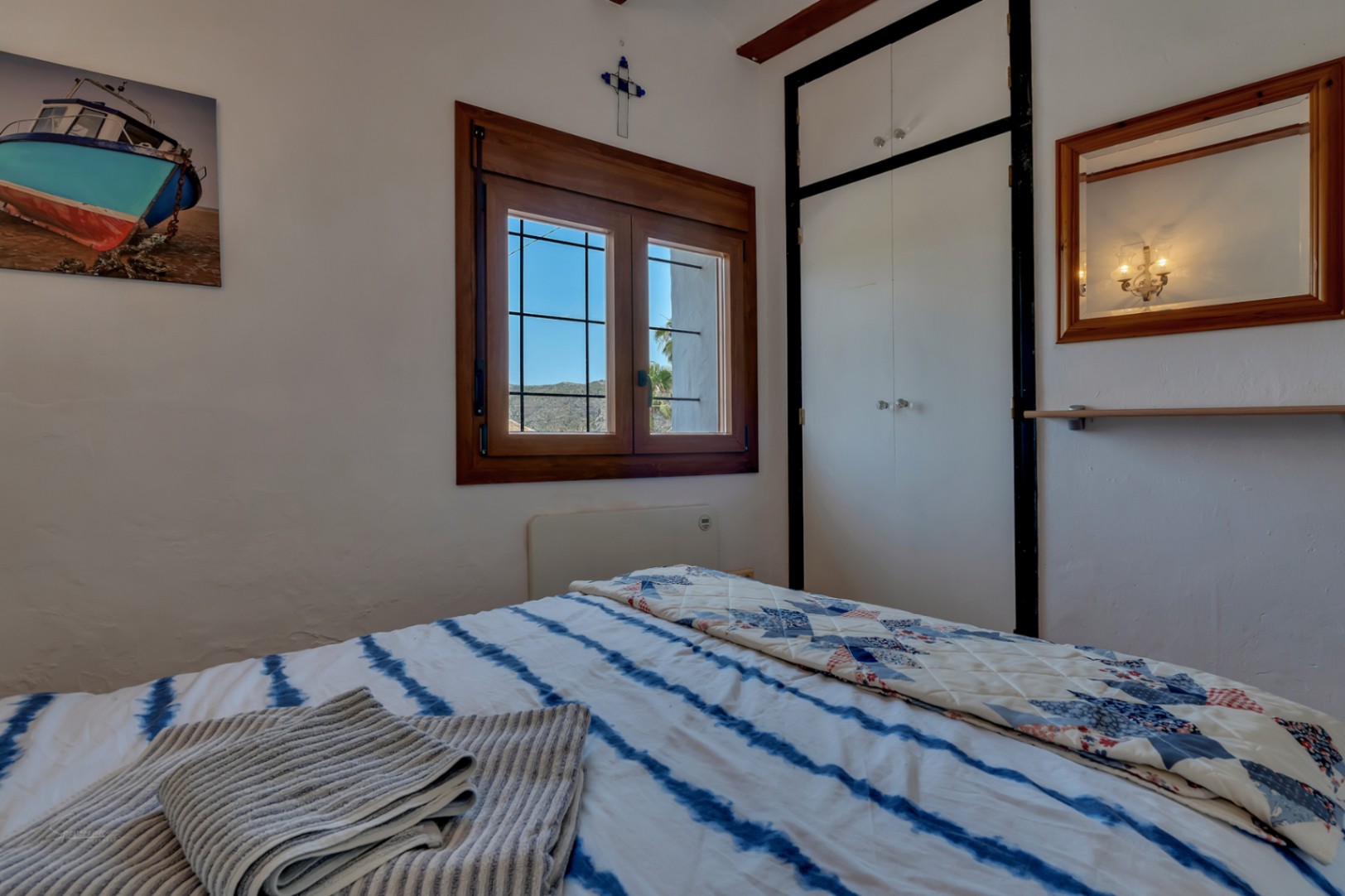 Bedroom with wood window, white closet, and blue striped bedding. Rustic decor and bright atmosphere.