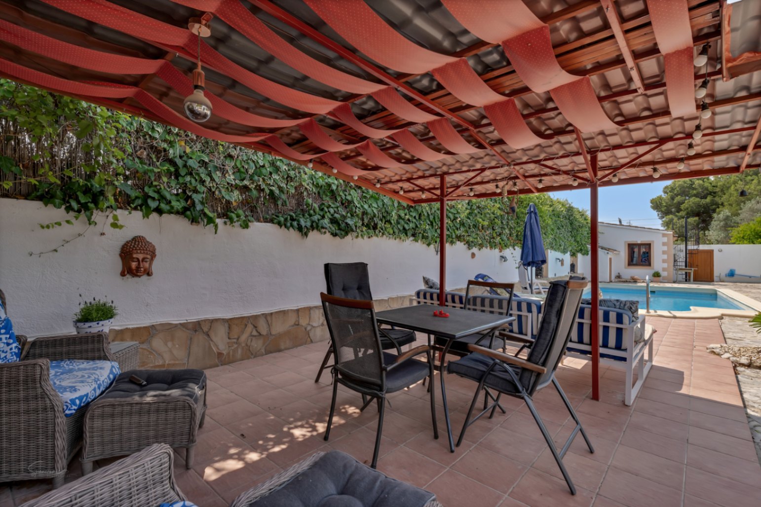 Covered terrace with red awning and tile floor. White wall with Buddha decor and vertical garden.
