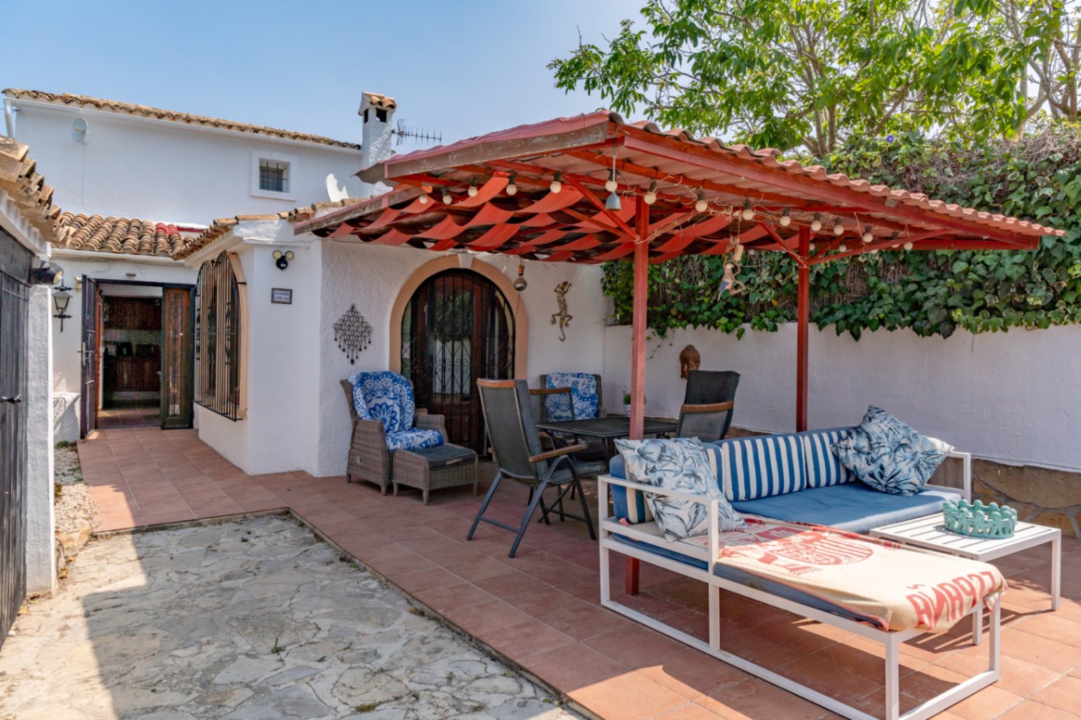 Covered terrace with red awning, garden furniture, and access to the country house in Teulada.