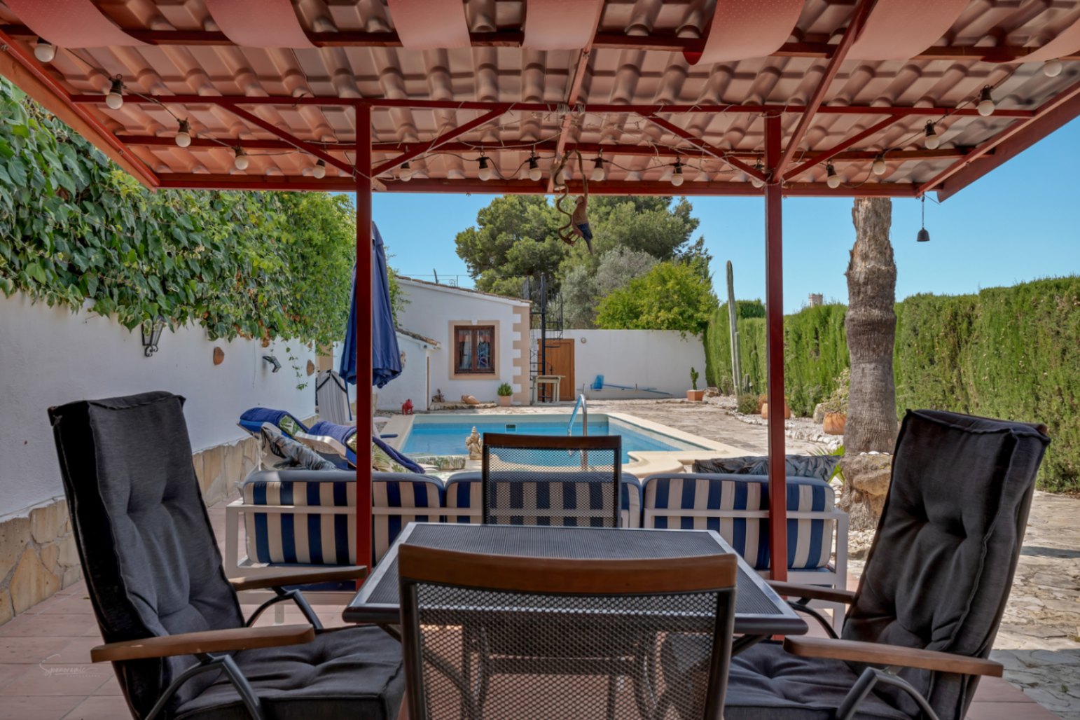 Pool-view porch. Wicker chairs with dark cushions under a red tile roof.