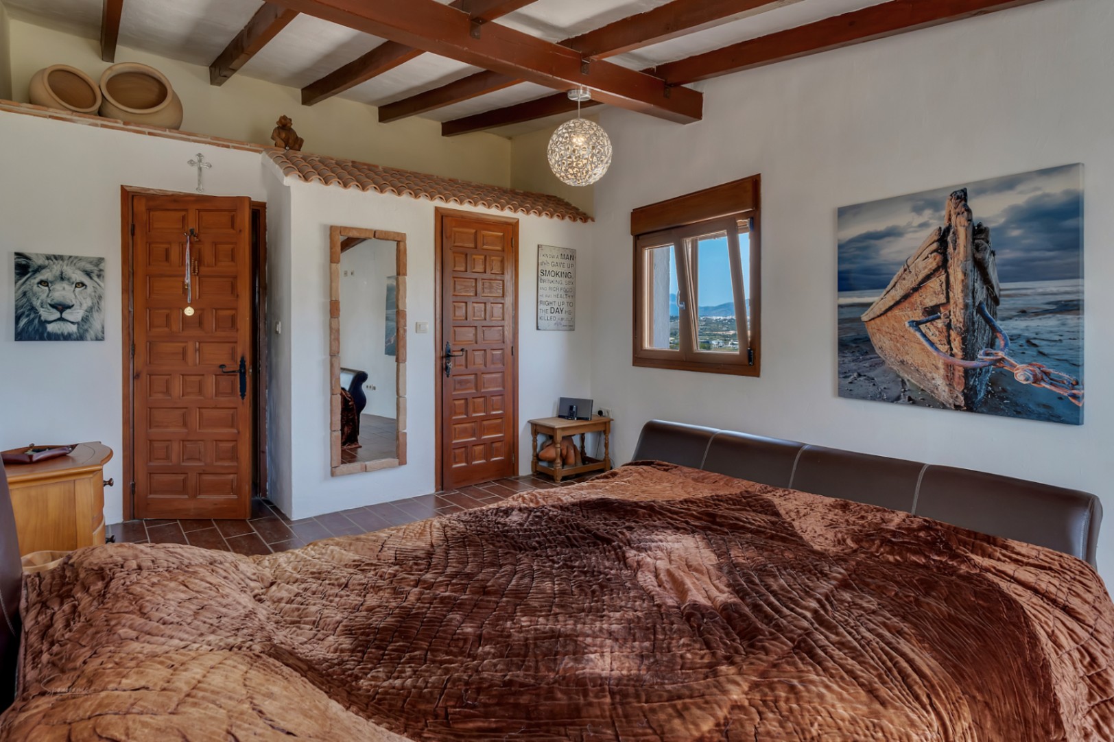 Rustic bedroom featuring wood beams, tile flooring and a bed with a brown leather headboard.