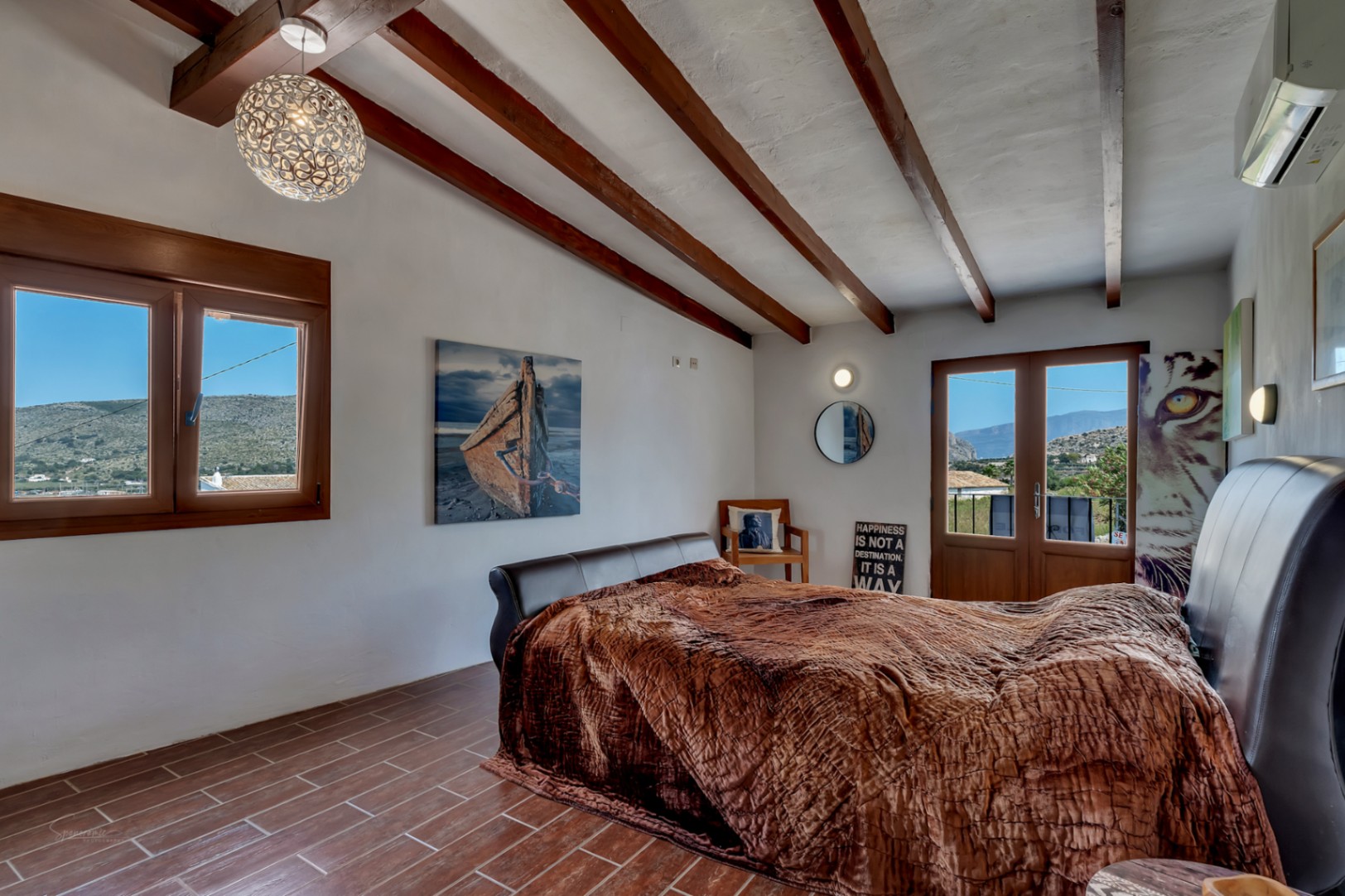 Rustic bedroom with wood beams, tile floor, and mountain view.