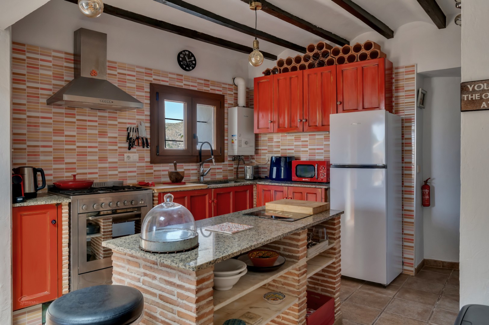 Rustic kitchen featuring granite countertops, red cabinets, and a brick central island with open shelving.