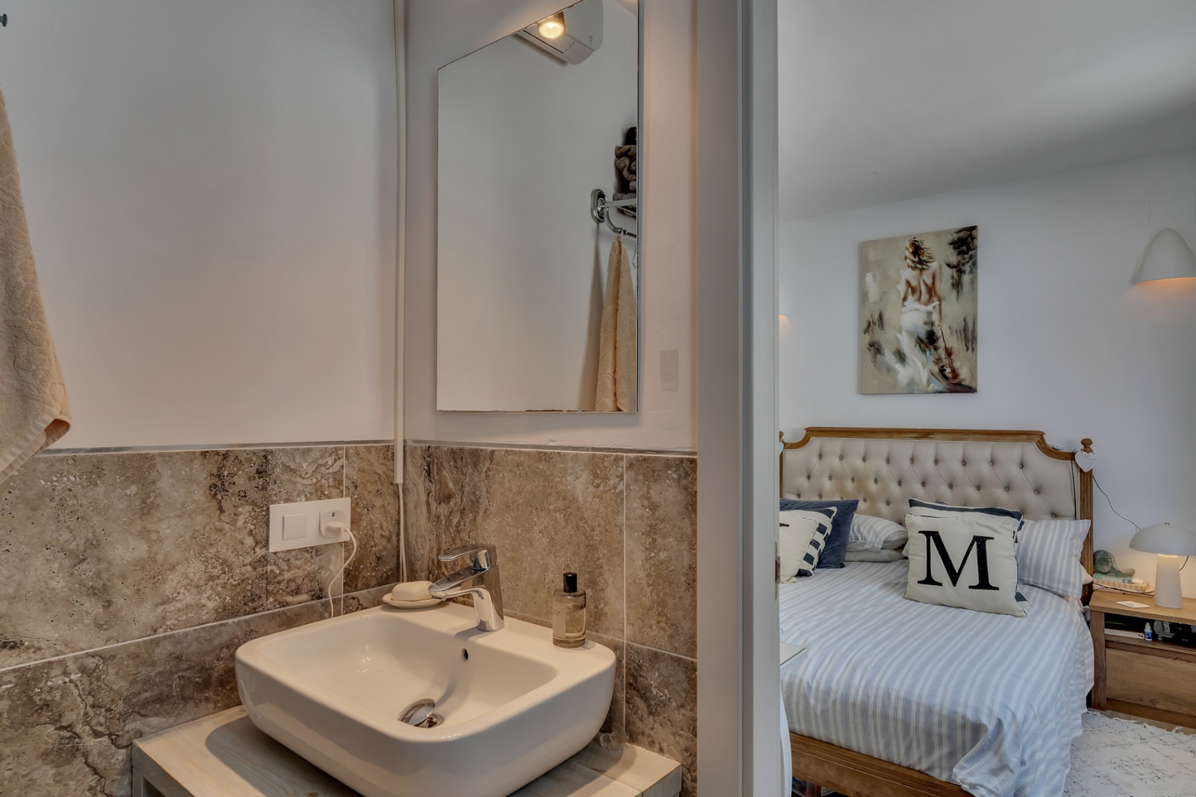 Bathroom detail with wood countertop and marble wall. Bedroom with upholstered headboard in the background.