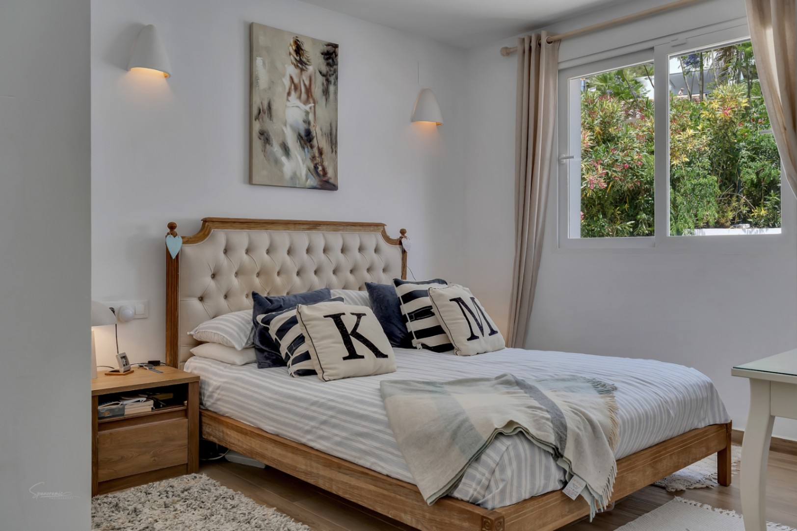 Bright bedroom featuring a wooden bed with upholstered headboard. Neutral decor and natural light.
