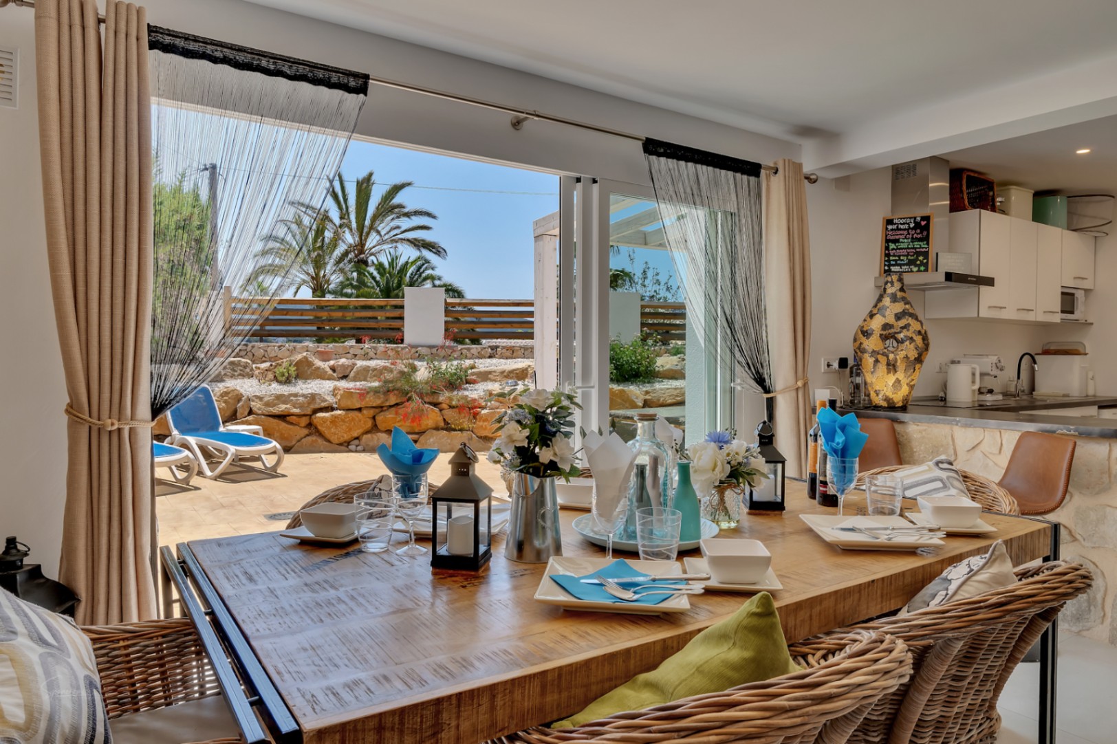 Bright dining room with rustic table and access to a terrace with sun loungers and Mediterranean garden.