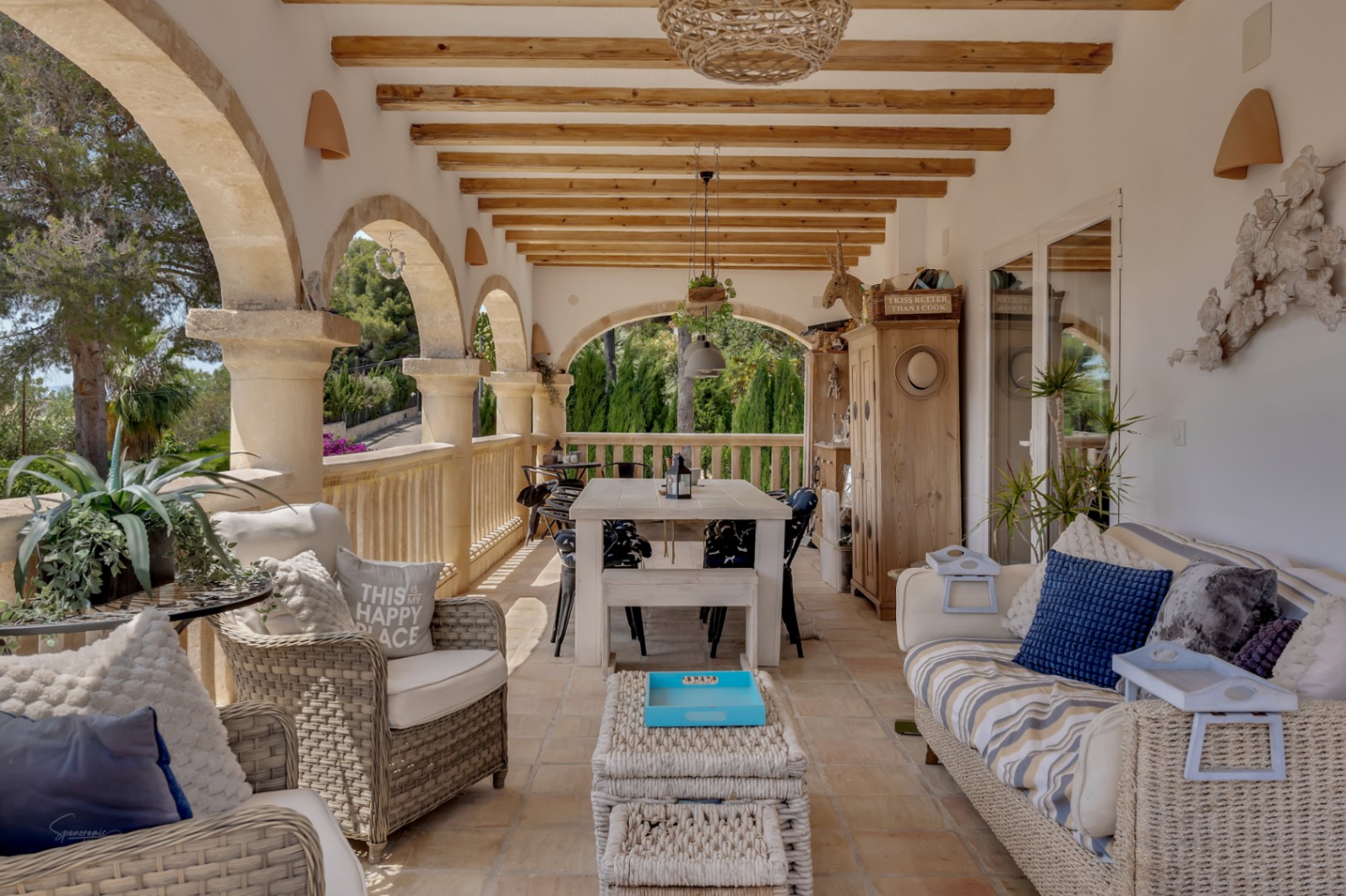 Porch with stone arches, wood beams and rattan furniture, creating a bright and inviting outdoor space.
