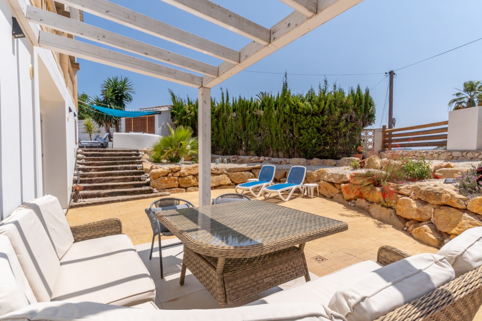 Terrace with white pergola, rattan furniture, and garden views with blue sun loungers.