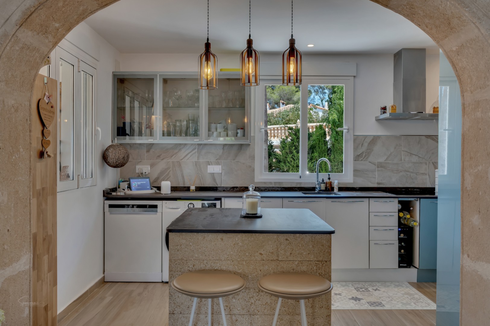 View of the modern kitchen featuring a stone island and designer pendant lights.