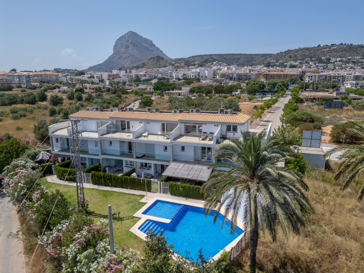 Aerial view of the modern residential complex featuring a communal pool, private patios, and a backdrop of the Montgó mountain and Jávea town.