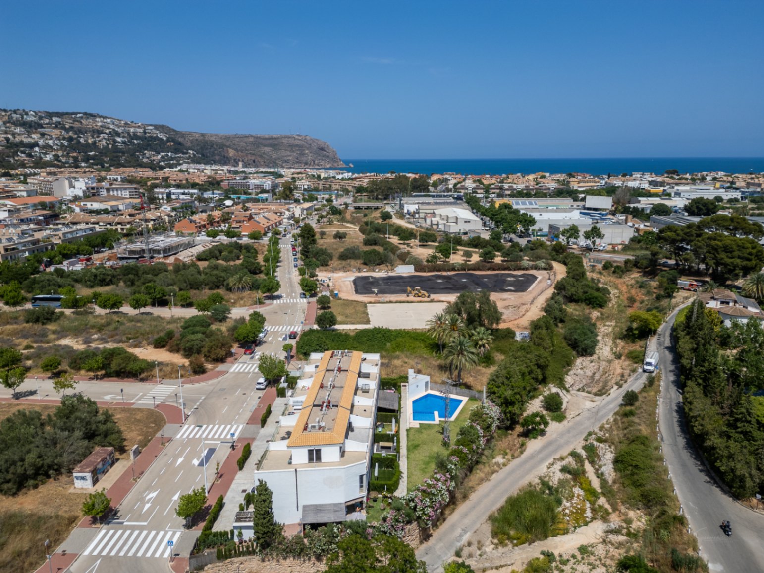 Aerial view of the modern residential complex featuring a communal pool, situated in a developing area of Jávea with distant Mediterranean Sea views.