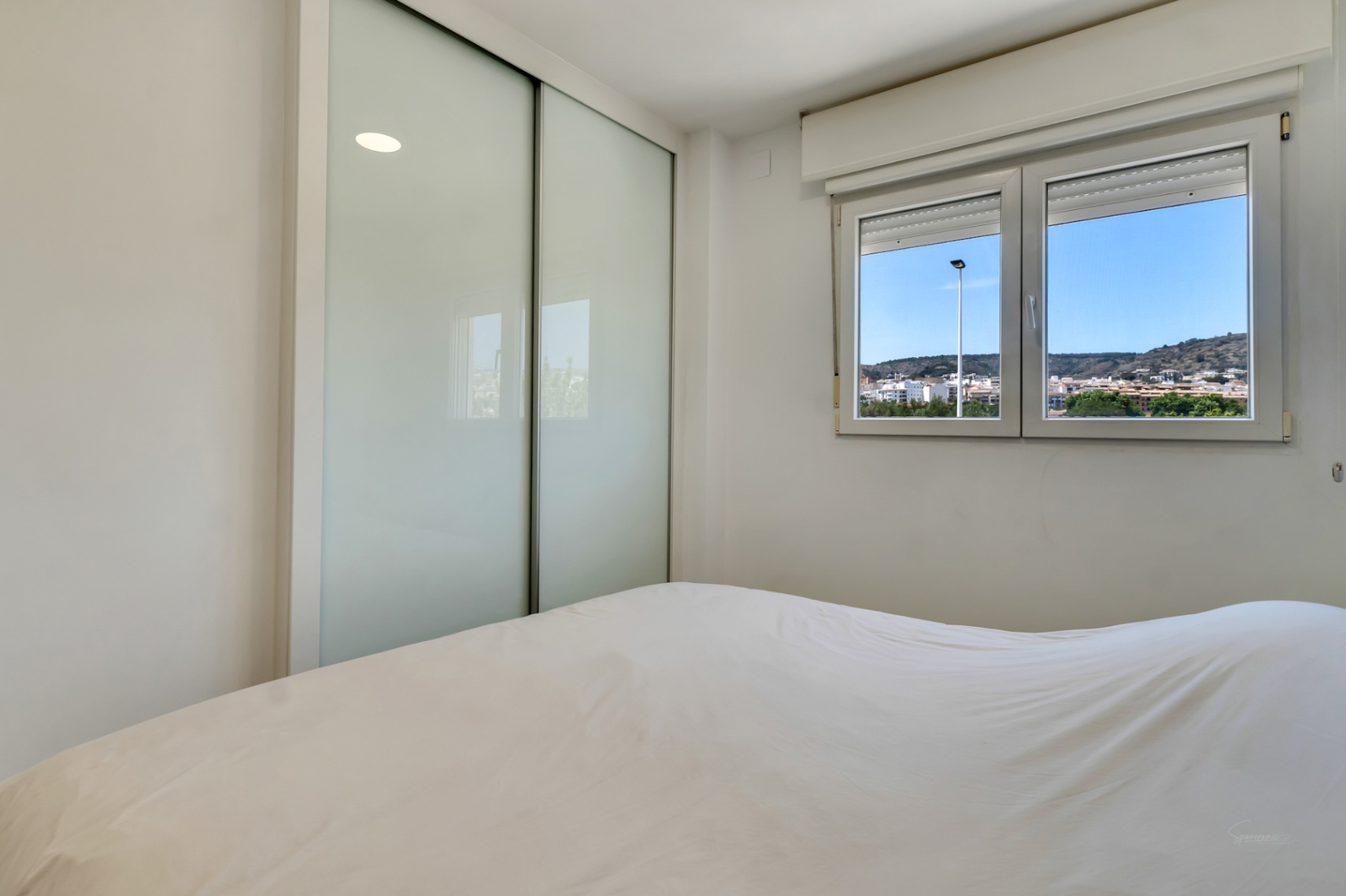 Bright bedroom featuring a built-in wardrobe with frosted glass sliding doors and a double-glazed window offering views of the surrounding hills.