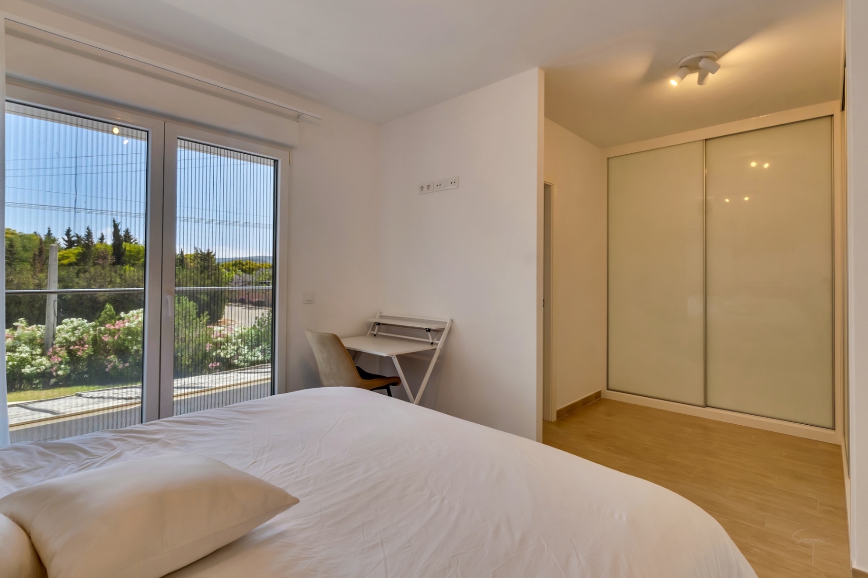Bright bedroom featuring a built-in wardrobe with sliding doors, a dedicated workspace, and large glass doors with a mosquito screen opening to the outdoors.