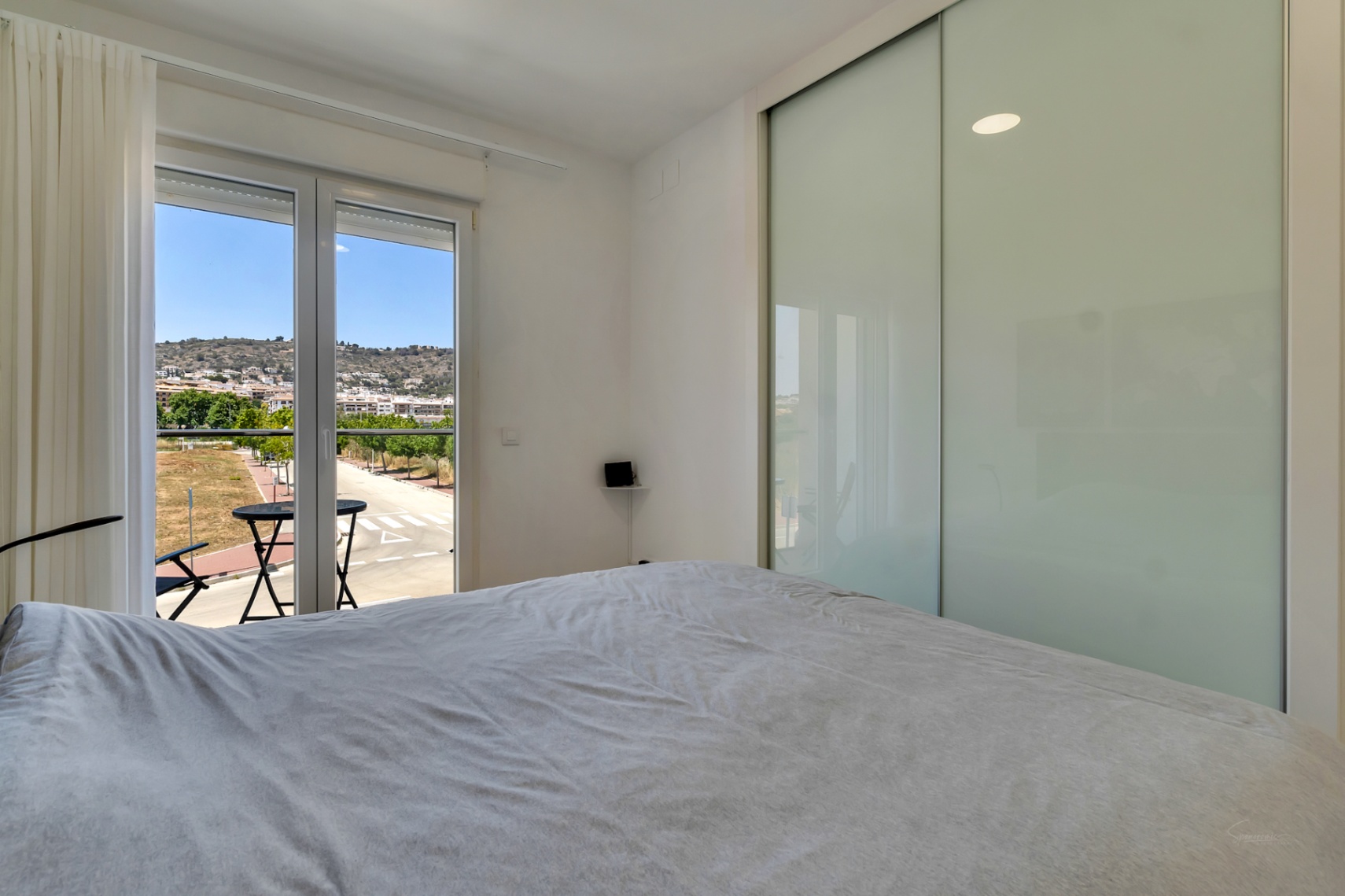 Bright bedroom featuring a large built-in wardrobe with frosted glass sliding doors and a private balcony offering views of the surrounding hills.