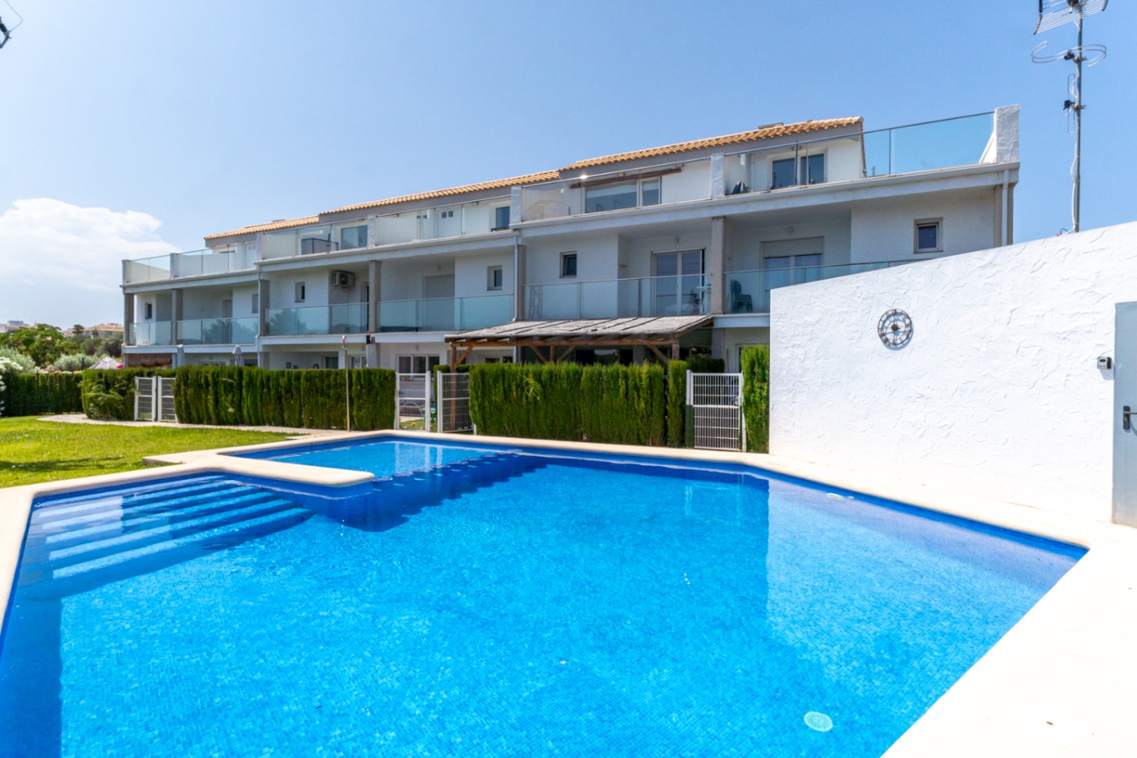Community swimming pool with blue tiling and integrated steps, set against the modern white facade of the townhouses featuring glass balconies and private patios.