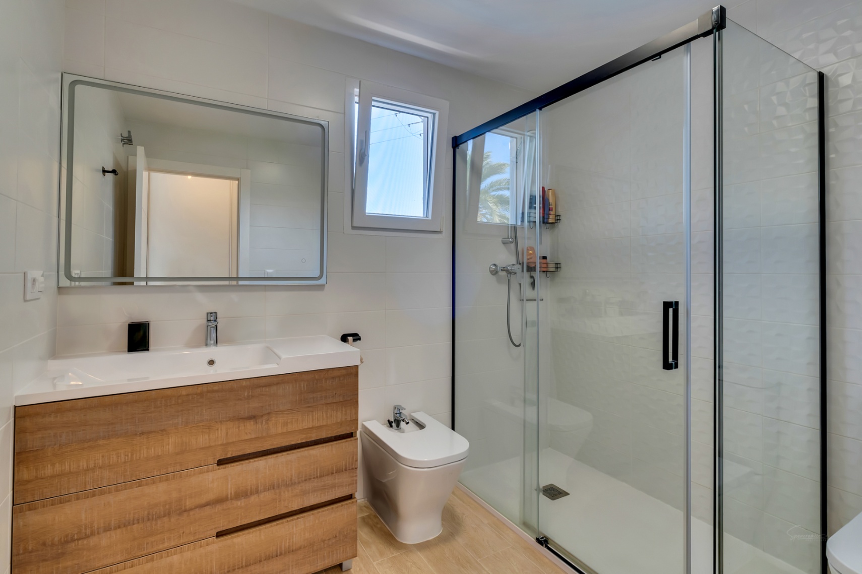 Contemporary bathroom featuring a wood-effect vanity, a white bidet, and a spacious walk-in shower with black-framed glass sliding doors and textured wall tiles.