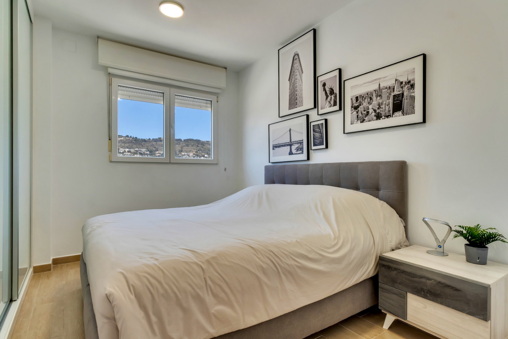 Double bedroom featuring a grey upholstered headboard, built-in wardrobes, and a window offering clear views of the Montgó mountain.