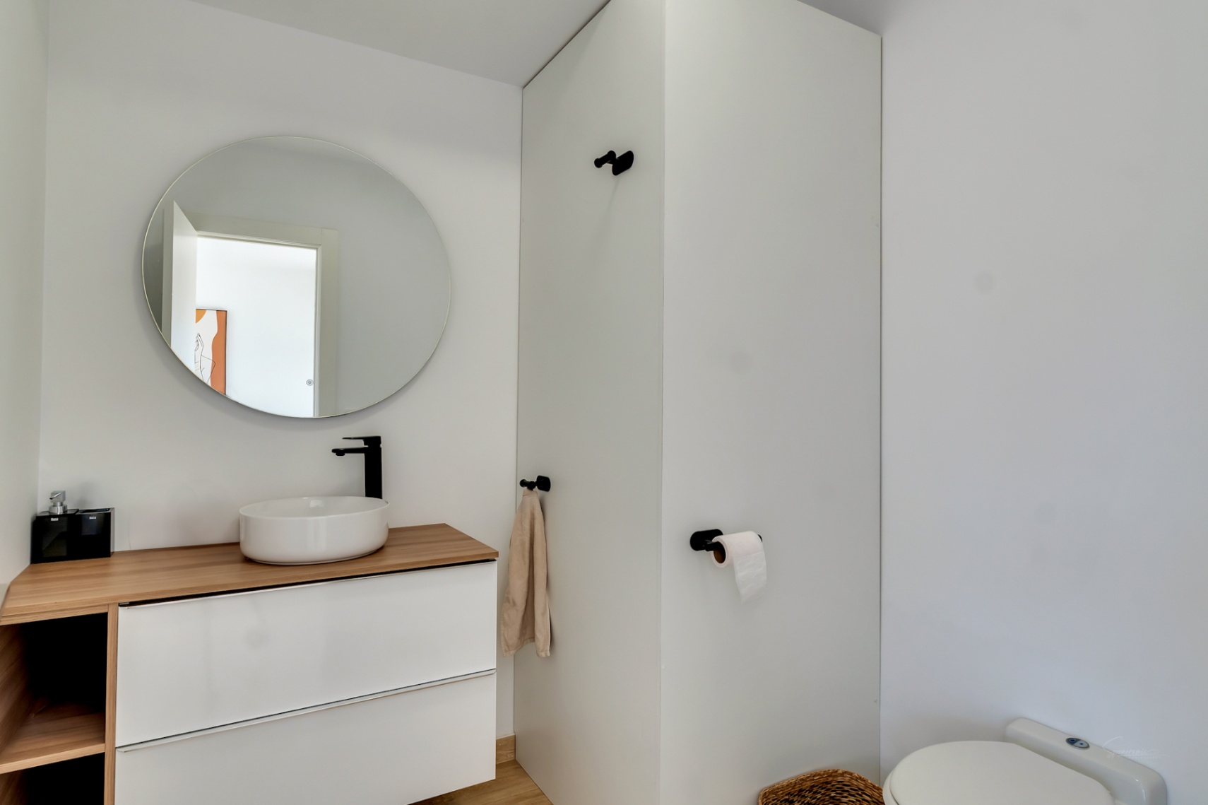 Modern bathroom featuring a vessel sink on a wooden countertop, matte black fixtures, and a circular mirror. The minimalist design incorporates clean white lines.