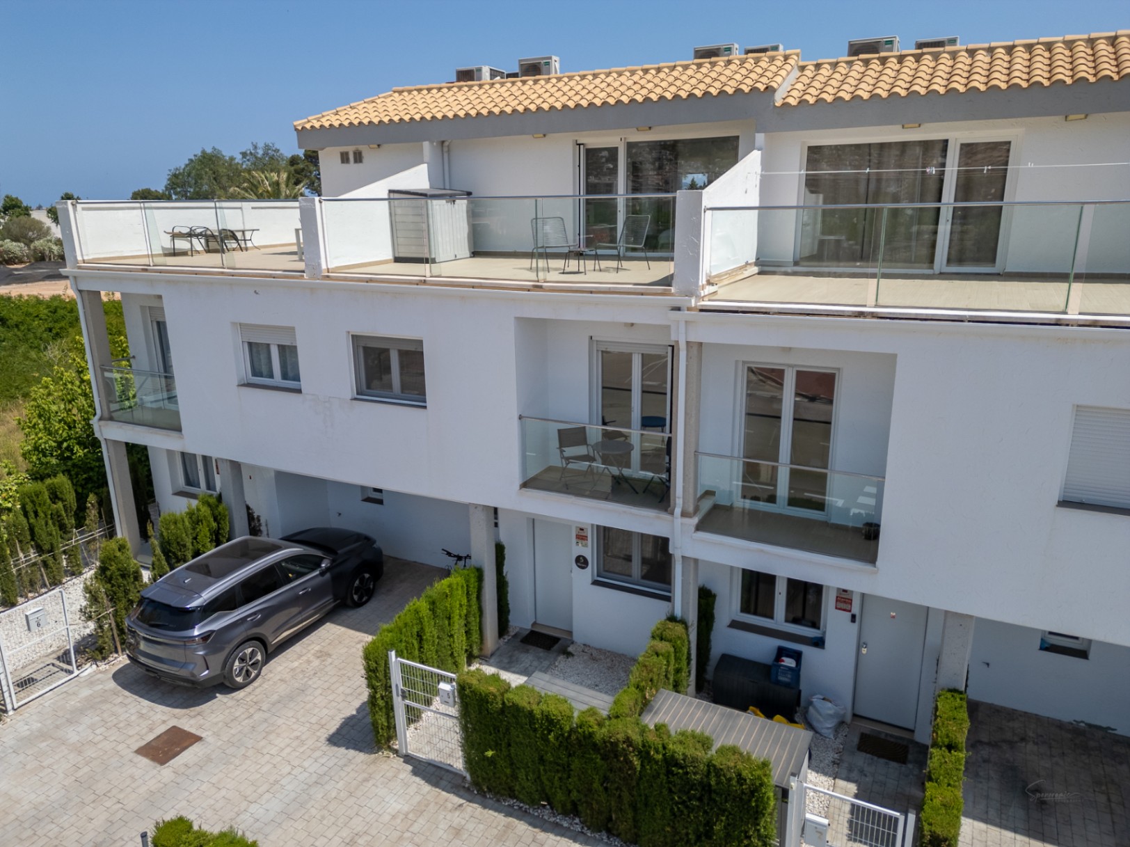 Modern three-story facade featuring spacious top-floor terraces with glass railings and private driveway parking at the entrance.