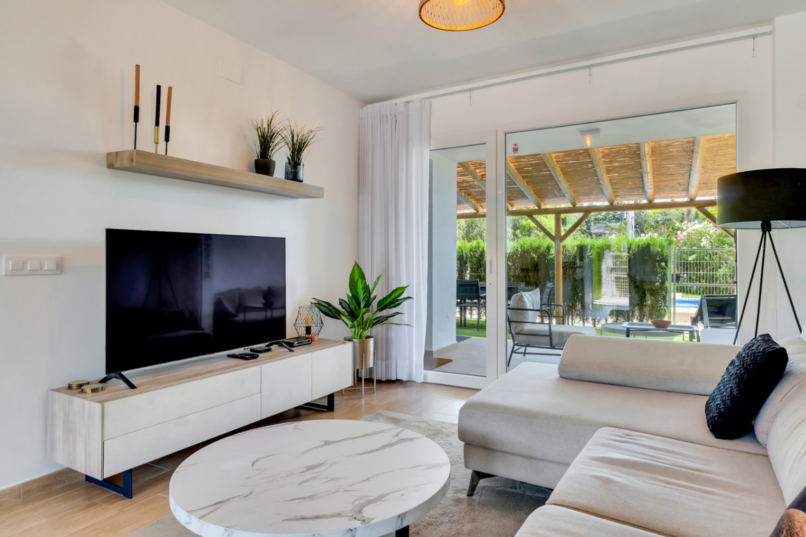 Open-concept living room featuring contemporary furniture and large glass doors that open directly onto a private patio with a wooden pergola.