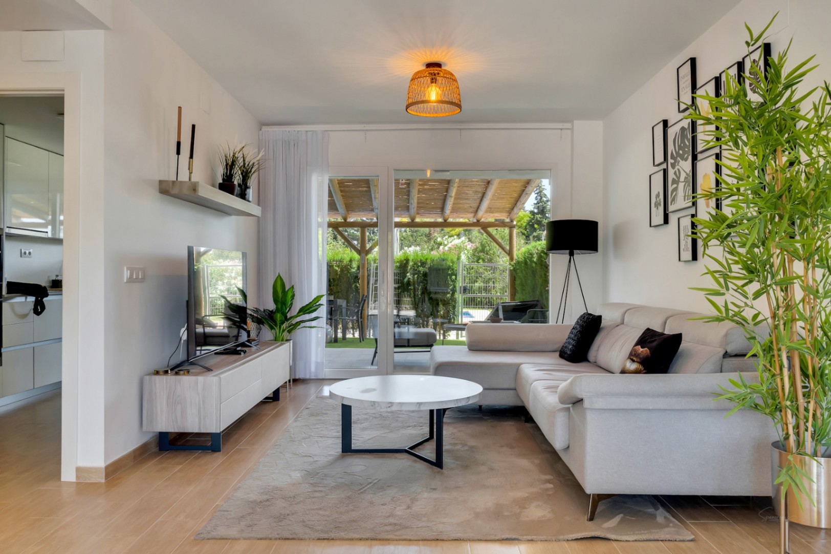 Open-concept living room featuring wood-effect flooring, contemporary furniture, and large sliding doors opening onto the private patio with a wooden pergola.
