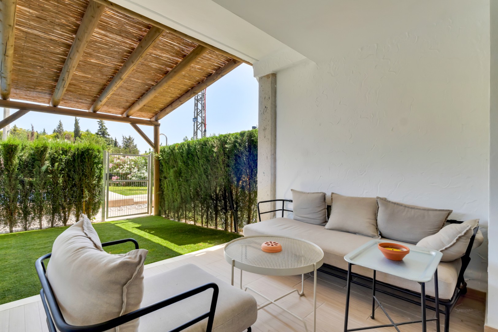 Private patio featuring a lounge area under a wooden pergola, artificial grass, and a secure gate providing direct access to the communal gardens.