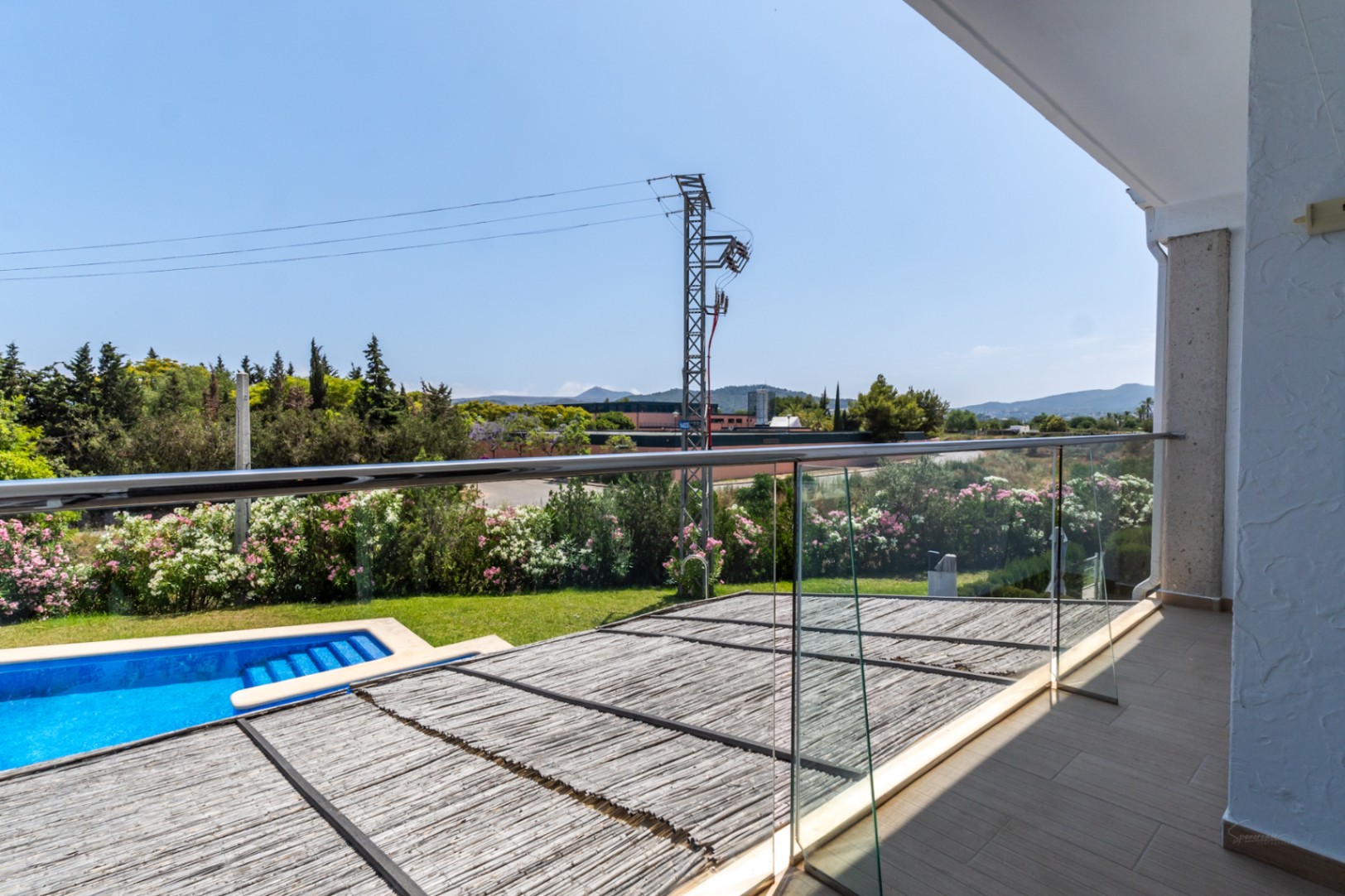 Upper terrace featuring a glass balustrade with views over the private patio's reed pergola, the swimming pool, and the surrounding Mediterranean landscape.