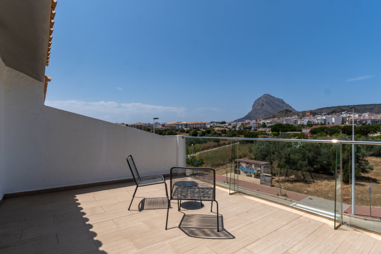 Upper terrace featuring a glass railing and panoramic views of the Montgó mountain and Jávea. Equipped with modern metal seating and light-toned flooring.