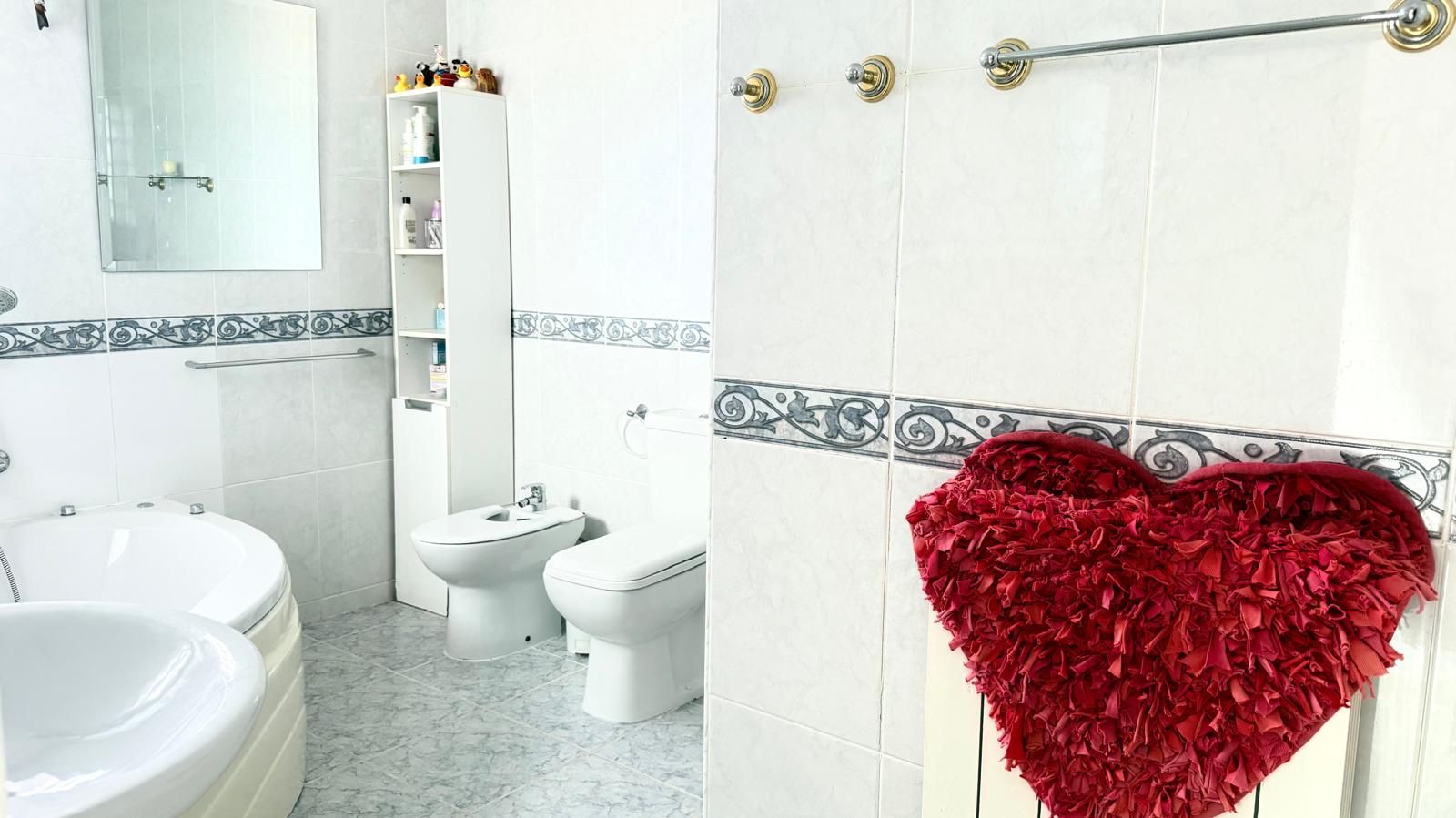 Bathroom featuring a corner whirlpool bathtub, bidet, and toilet, with white tiled walls accented by a decorative border and gold-toned fixtures.