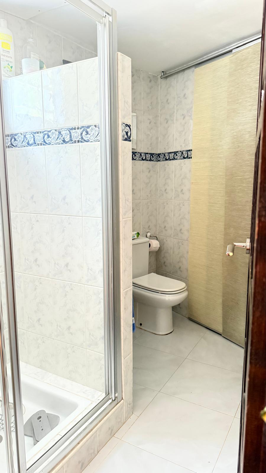 Bathroom featuring a glass shower enclosure, white wall tiles with a blue decorative border, and a white ceramic toilet. A textured sliding door completes the space.