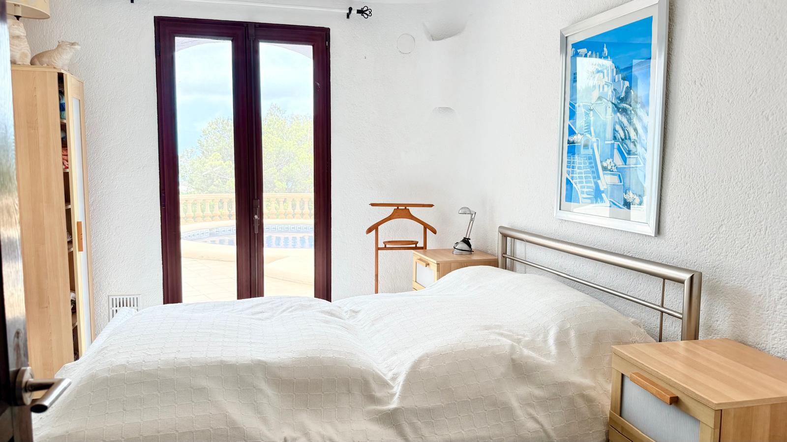 Bedroom featuring direct access to the pool terrace, textured white walls, wooden bedside furniture, and a metal headboard under natural light.