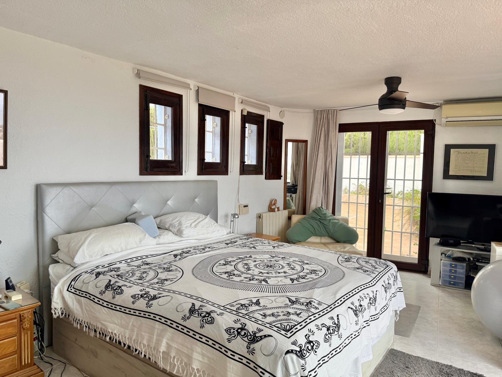 Bright master bedroom featuring dark wood frames, a ceiling fan, and large glass doors offering direct access to the outdoor terrace area.