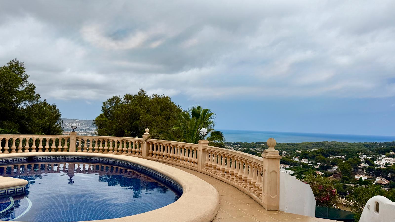 Circular pool with blue mosaic tiling and a classic stone balustrade, featuring panoramic views of the Mediterranean Sea and Jávea's coastal landscape.