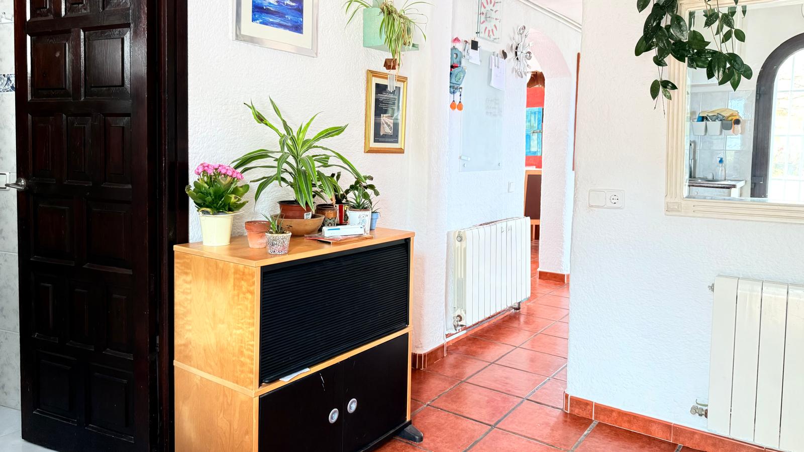 Entrance hallway featuring traditional terracotta floor tiles, white textured walls, central heating radiators, and a dark wood paneled door.
