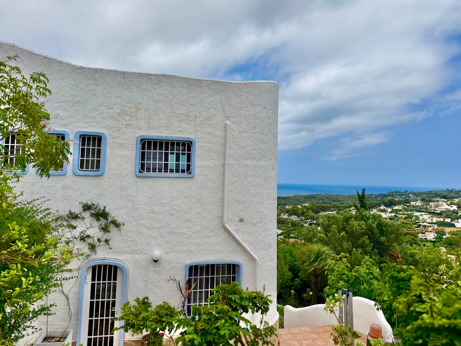 Ibicencan-style facade featuring textured white walls, blue-trimmed windows with security bars, and panoramic views over the Mediterranean Sea and the Jávea coastline.