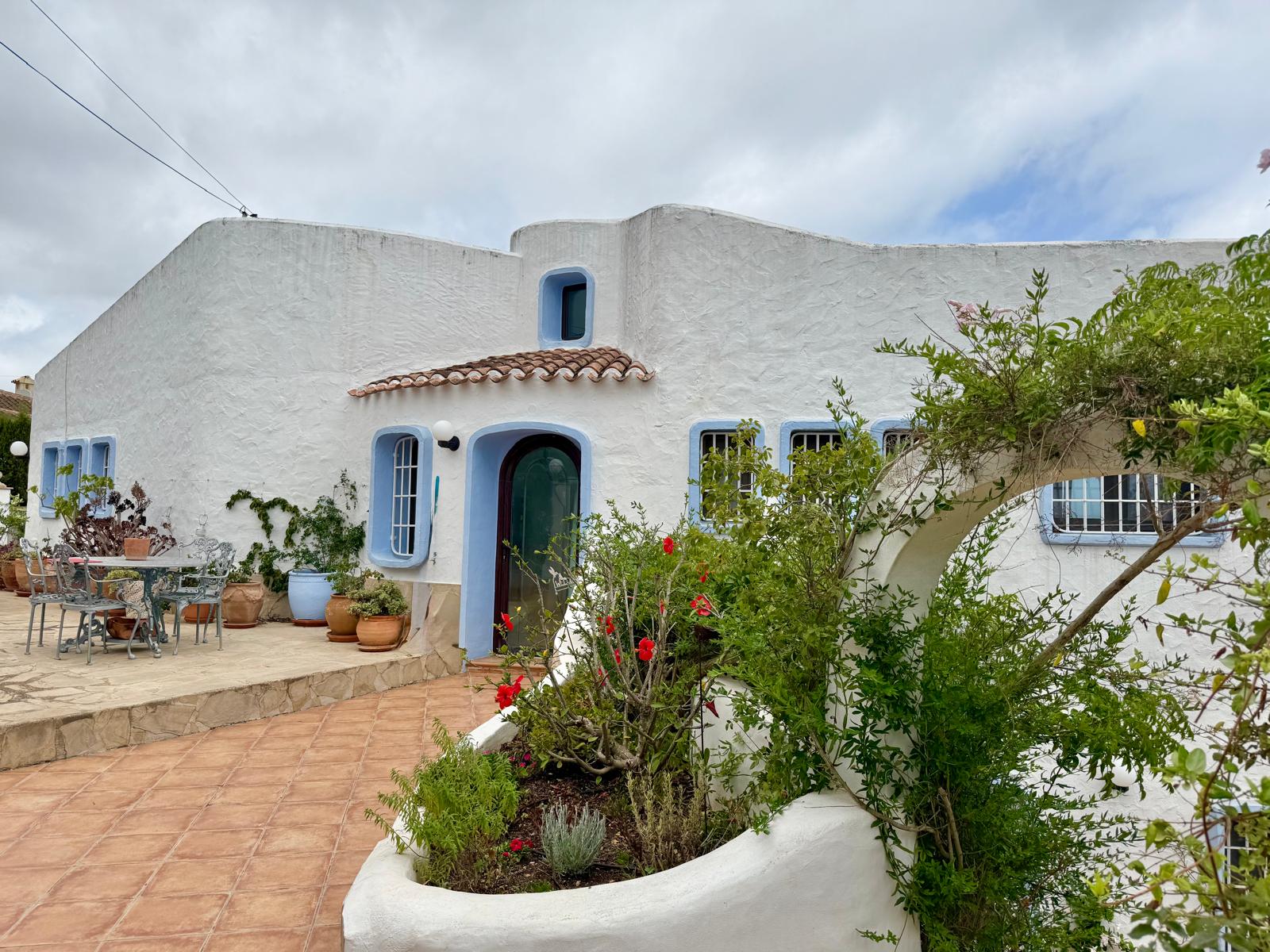 Ibicencan-style facade featuring white walls, blue-trimmed windows, and a terracotta tiled terrace with built-in planters and Mediterranean greenery.