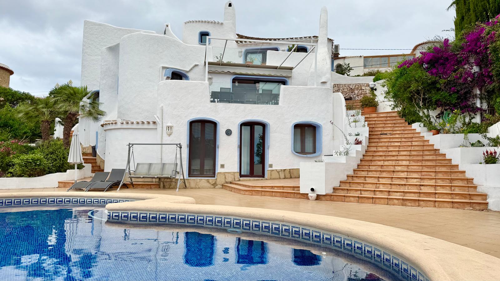 Ibizan-style facade with organic white forms and terraced levels connected by exterior stairs, situated next to the swimming pool and garden.