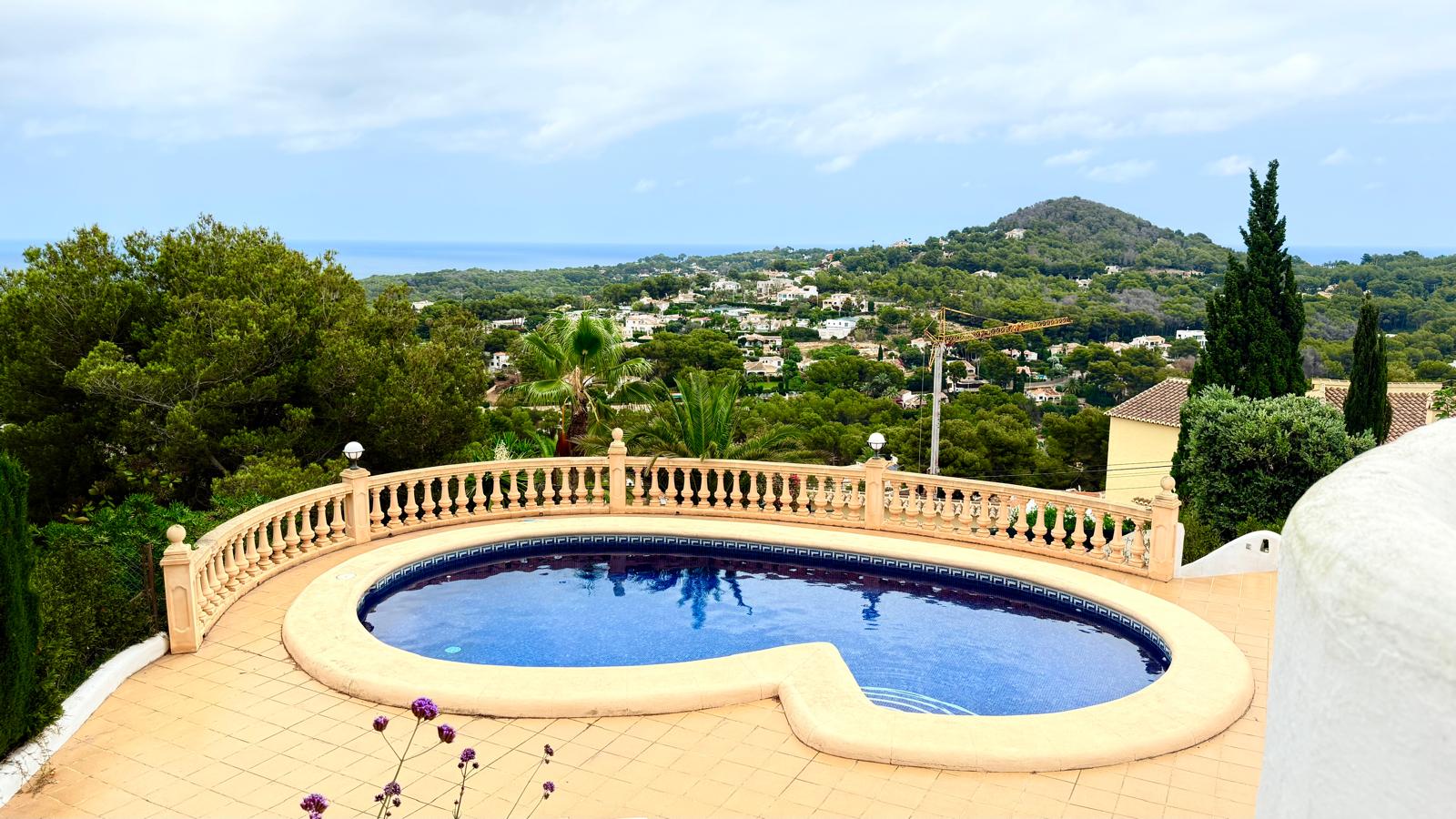 Kidney-shaped private pool featuring blue mosaic tiling and a stone balustrade, offering expansive views of the Mediterranean Sea and lush coastal landscape.